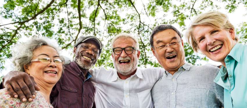 A smiling group of retirement-age people stand with their arms around one another's shoulders.