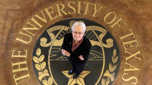 Diana Natalicion standing on the seal of The University of Texas on a floor, looking up at a camera.