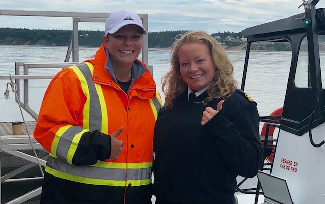 Angel Lemmonds stands next to a uniformed woman on a boat, but giving 'thumbs up.'