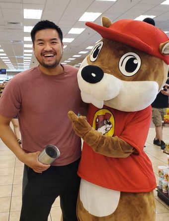 Justin Tam inside a Buck-ees store standing alongside a life-sized mascot.