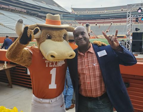 Archie Holmes, UT System's Executive Vice Chancellor for Academic Affairs, gives the hook 'em sign standing next to UT Austin mascot Hook 'Em.