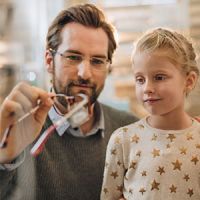 Photo of a middle-aged dad showing a pair of glasses to his daughter